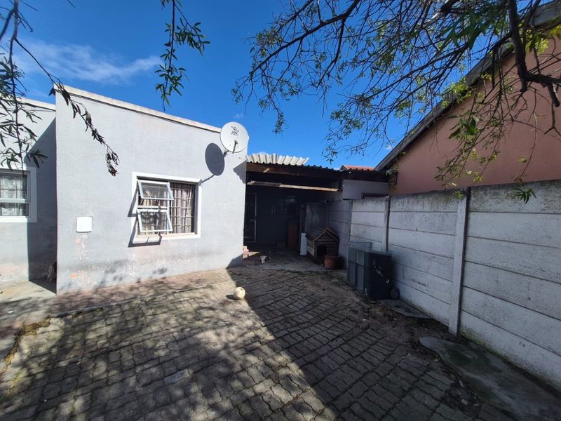A rear courtyard featuring paved flooring, a precast concrete boundary wall, and a small covered patio area attached to the main dwelling.