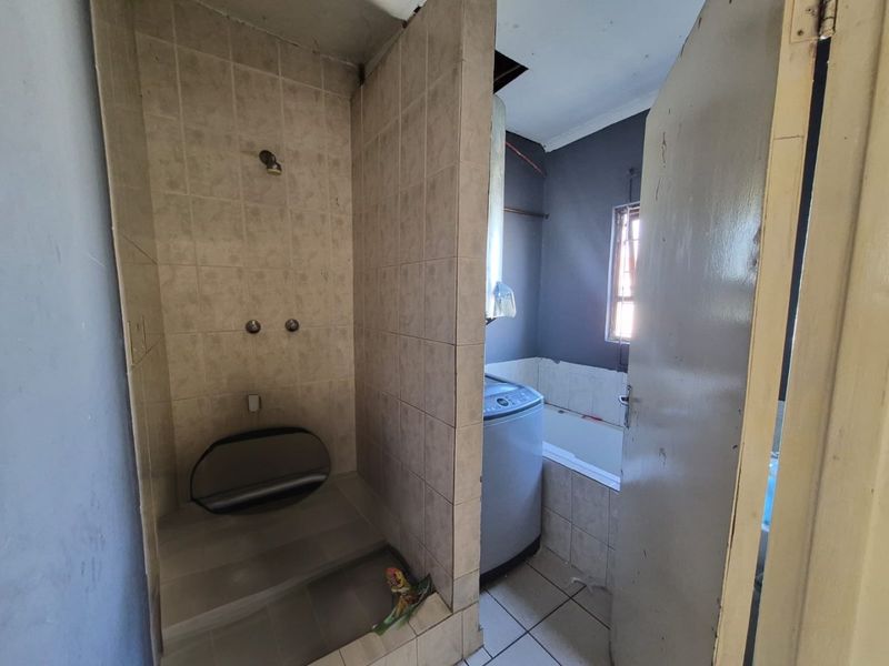 A dated bathroom featuring a tiled shower enclosure and a built-in bathtub, requiring renovation to update the finishes and address ceiling damage.