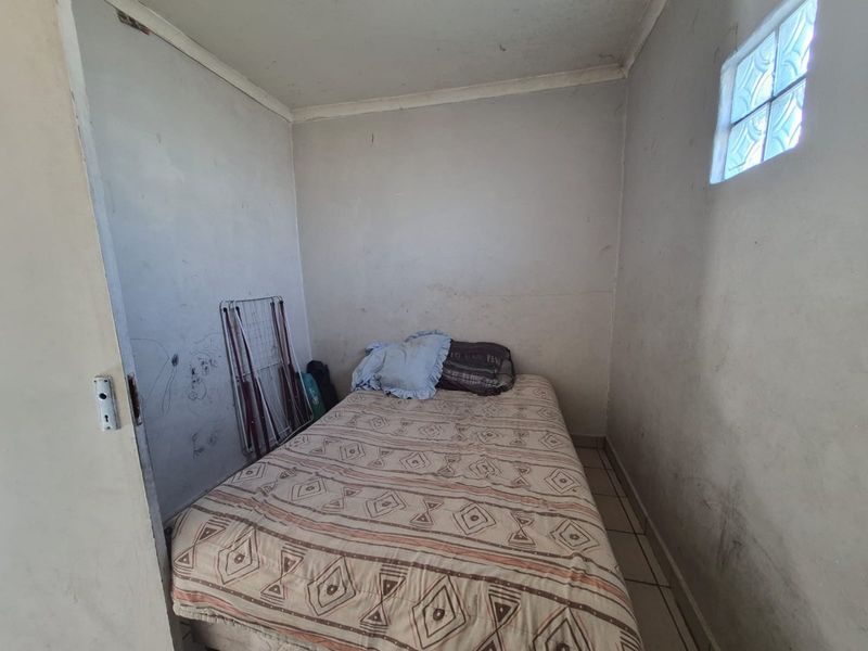 A small bedroom featuring tiled flooring and a glass block window, currently requiring wall repairs and fresh paint to improve its condition.