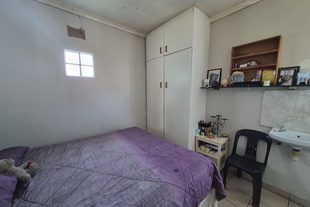Bedroom featuring a built-in wardrobe, tiled flooring, and a wall-mounted basin, showing signs of wear and ceiling damage.