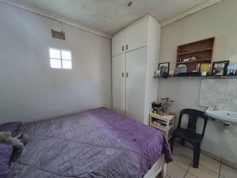 Bedroom featuring a built-in wardrobe, tiled flooring, and a wall-mounted basin, showing signs of wear and ceiling damage.