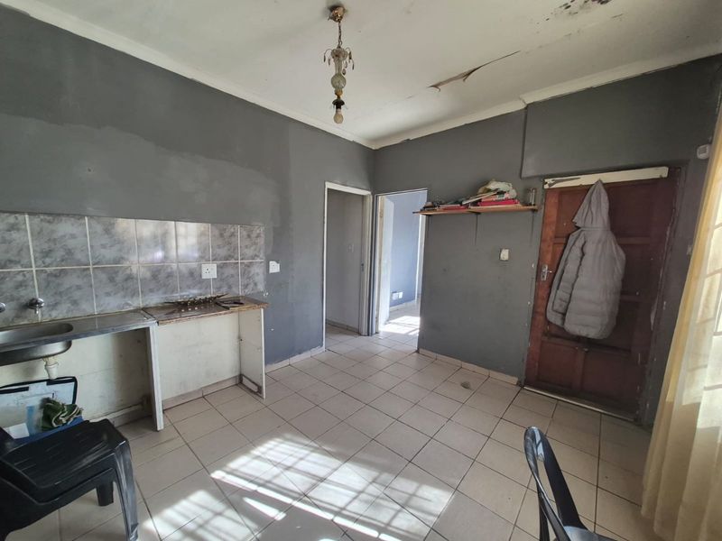 A basic kitchen area featuring tiled flooring, a stainless steel sink, and a tiled backsplash, currently requiring cosmetic repairs and ceiling maintenance.