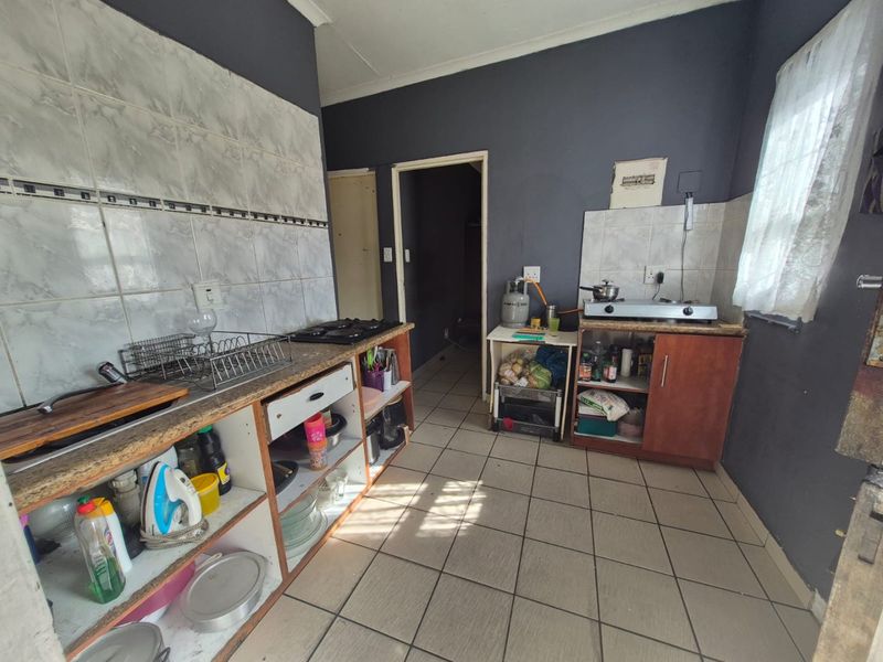 A functional kitchen featuring tiled flooring, a tiled splashback, and built-in cabinetry with a gas hob, offering potential for modernization and cosmetic updates.