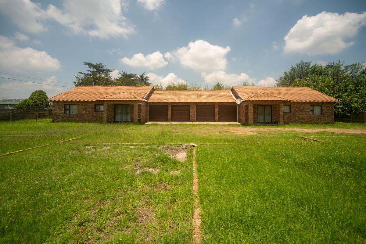 Rear view of a face brick house featuring four garage doors, sliding glass access points, and a large, expansive lawn area.