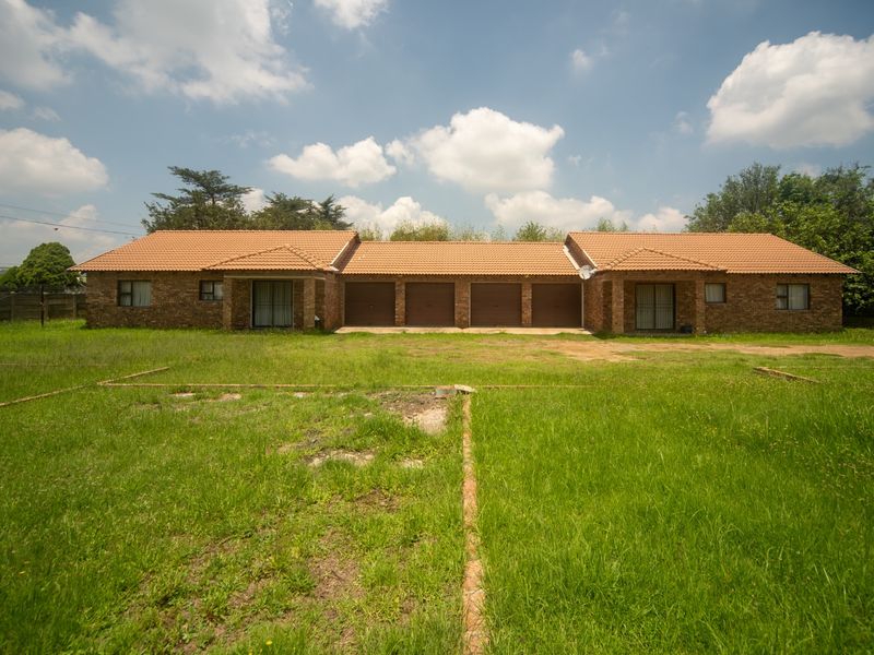 Rear view of a face brick house featuring four garage doors, sliding glass access points, and a large, expansive lawn area.