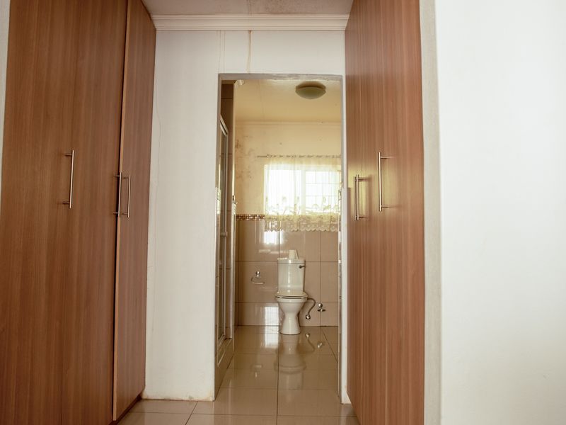 A view through a hallway with built-in cupboards into a bathroom featuring tiled floors, a toilet, and a shower enclosure.