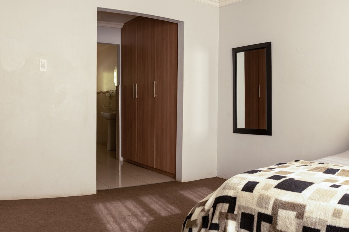A bedroom featuring built-in cupboards and carpeted flooring, with an adjoining en-suite bathroom visible through the doorway.