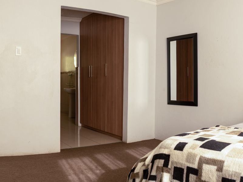 A bedroom featuring built-in cupboards and carpeted flooring, with an adjoining en-suite bathroom visible through the doorway.