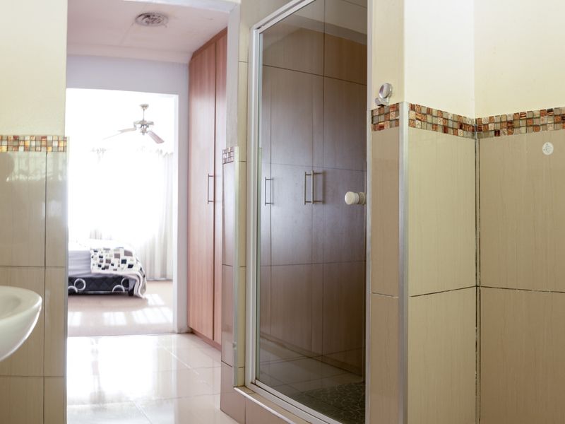 Bathroom featuring a shower enclosure, tiled finishes, and a pedestal basin, with a view into an adjacent bedroom with built-in storage.