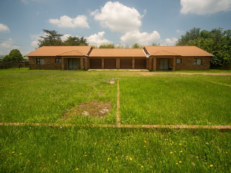 Rear view of a face brick residential property featuring four garage doors, sliding access points, and a large, expansive lawn area.