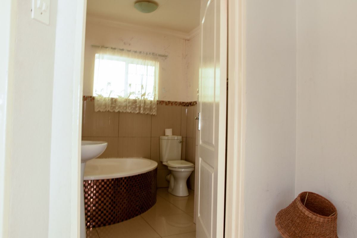 A compact bathroom featuring a pedestal basin, built-in bathtub, and toilet, with tiled finishes and visible signs of wear on the walls.