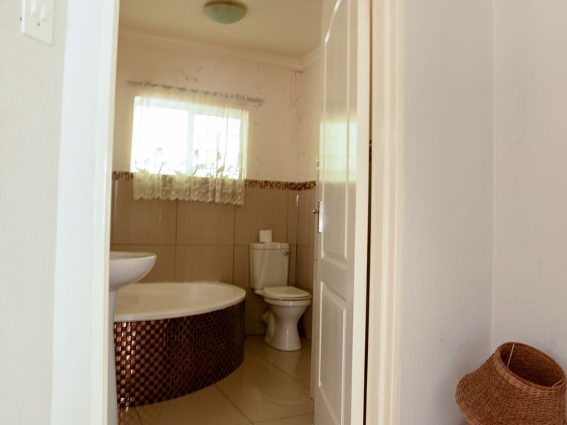 A compact bathroom featuring a pedestal basin, built-in bathtub, and toilet, with tiled finishes and visible signs of wear on the walls.