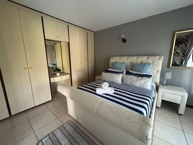 A bedroom featuring built-in cupboards with an integrated vanity mirror, tiled flooring, and a neutral wall finish.