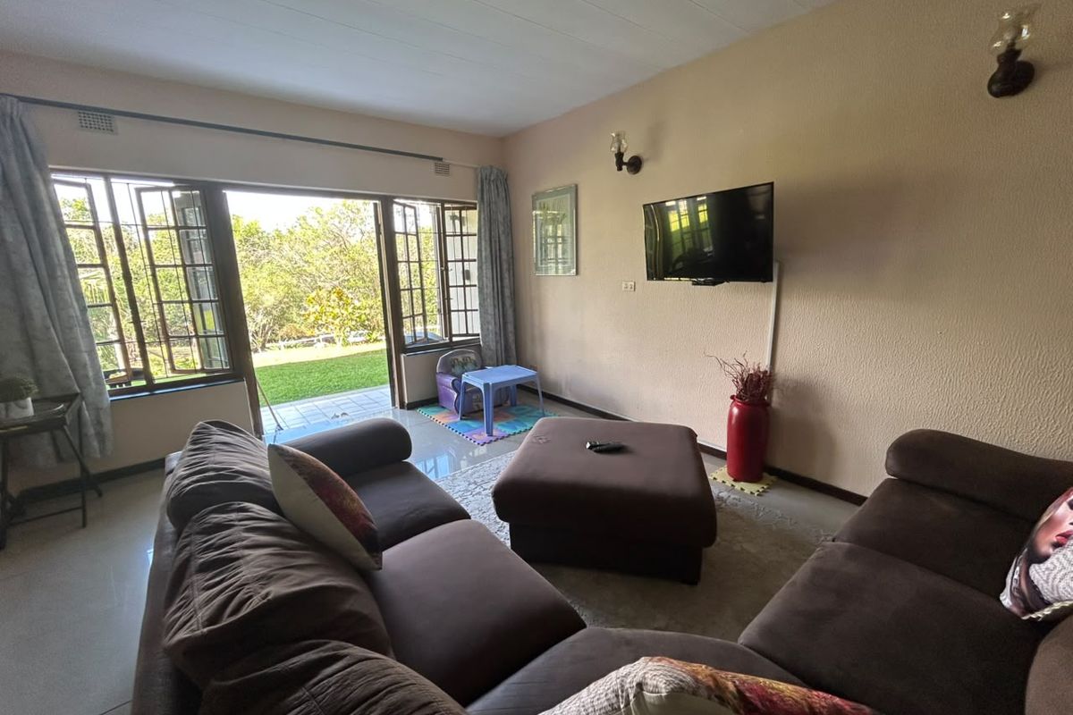 A living room featuring tiled floors, wall-mounted lighting, and a large sliding glass door providing direct access to the garden area.