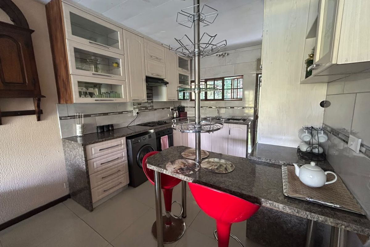 Functional kitchen featuring granite countertops, built-in cabinetry, an integrated oven and hob, and a breakfast bar area with tiled flooring.