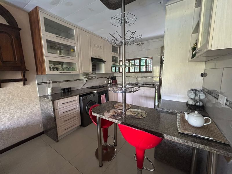 Functional kitchen featuring granite countertops, built-in cabinetry, an integrated oven and hob, and a breakfast bar area with tiled flooring.