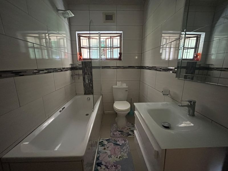 A well-maintained bathroom featuring a bathtub with a glass shower screen, a modern vanity with basin, and tiled walls.