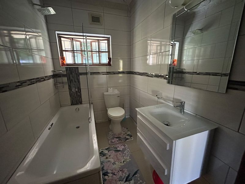 A well-maintained bathroom featuring a bathtub with shower head, a modern vanity unit with basin, and neutral wall tiling.