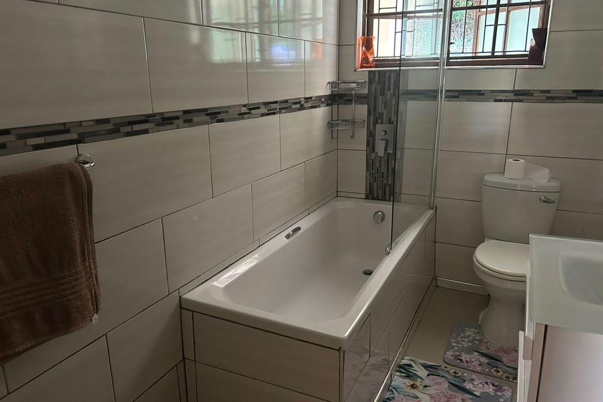 A functional bathroom featuring a bathtub with a glass screen, tiled walls with a decorative mosaic accent, and a standard toilet.