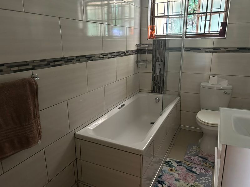 A functional bathroom featuring a bathtub with a glass screen, tiled walls with a decorative mosaic accent, and a standard toilet.