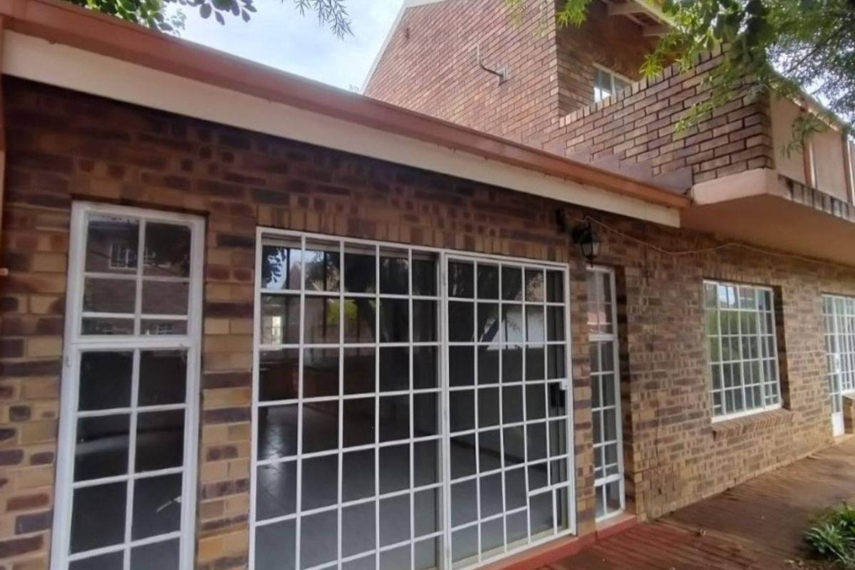 Rear exterior view of a face brick townhouse featuring sliding glass doors with security gates and a timber deck area.