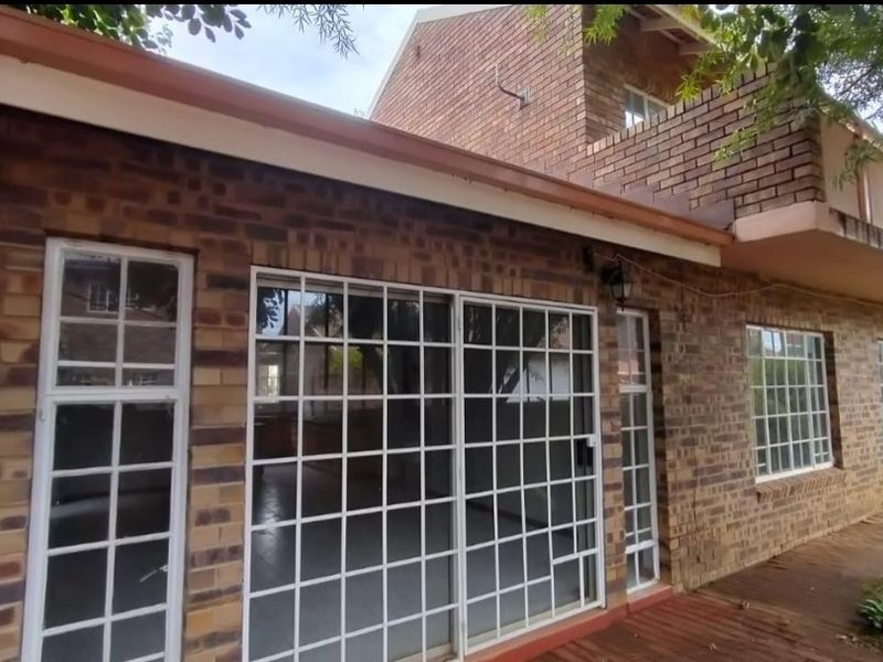 Rear exterior view of a face brick townhouse featuring sliding glass doors with security gates and a timber deck area.