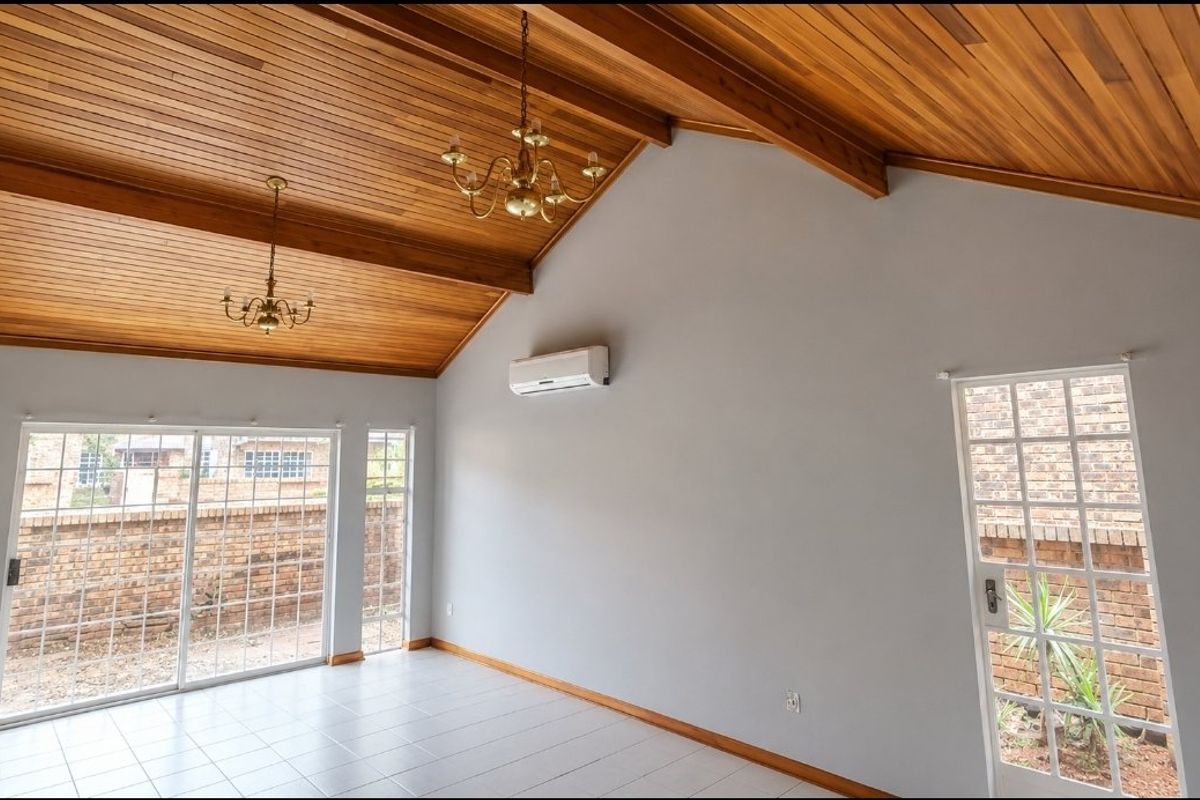 Spacious living area featuring a high vaulted timber ceiling with exposed beams, tiled flooring, split-system air conditioning, and direct access to the exterior.