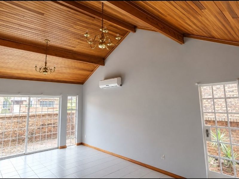 Spacious living area featuring a high vaulted timber ceiling with exposed beams, tiled flooring, split-system air conditioning, and direct access to the exterior.