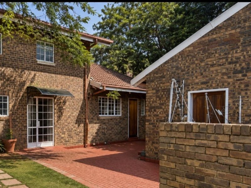 Rear exterior view of the townhouse featuring a face brick facade, paved patio area, and established garden surroundings.