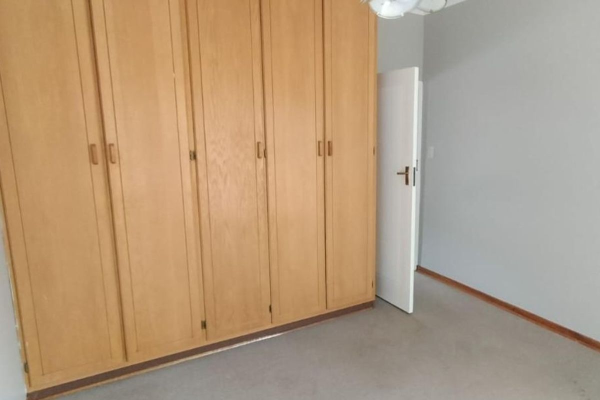 A vacant bedroom featuring floor-to-ceiling wooden built-in cupboards, neutral wall finishes, and carpeted flooring.