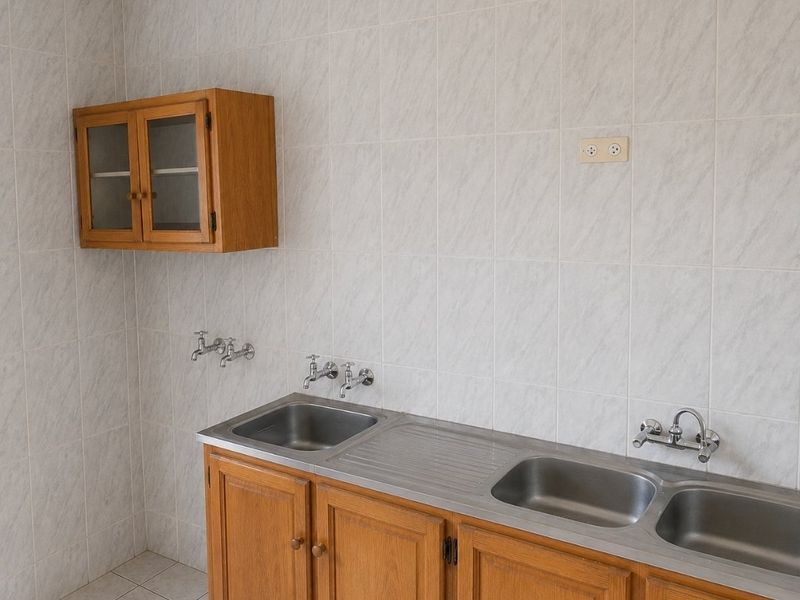 A functional laundry area featuring a stainless steel double sink, wall-mounted wooden cabinetry, and tiled finishes throughout.