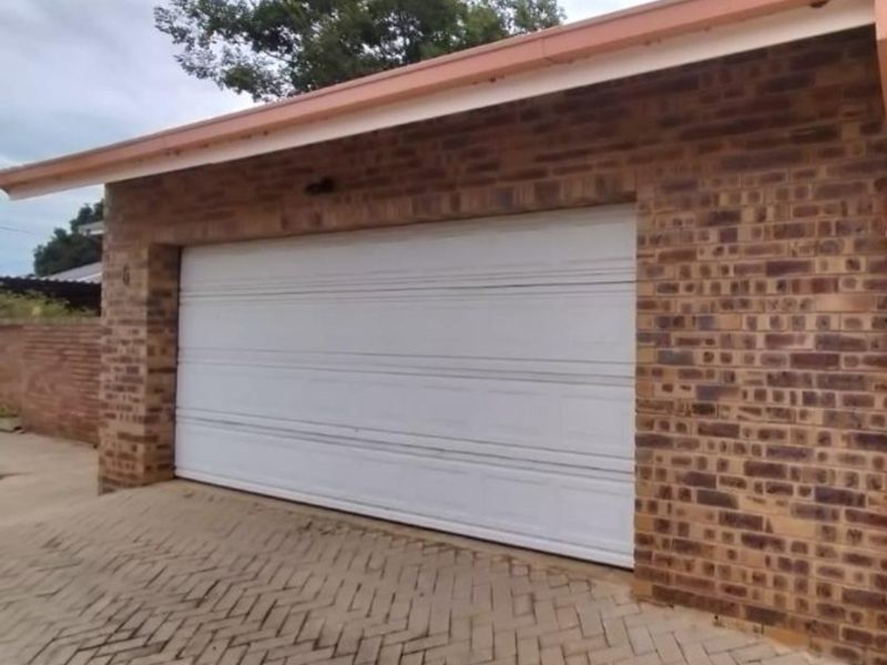 A single-car garage featuring a white sectional door, face-brick exterior walls, and a paved driveway.