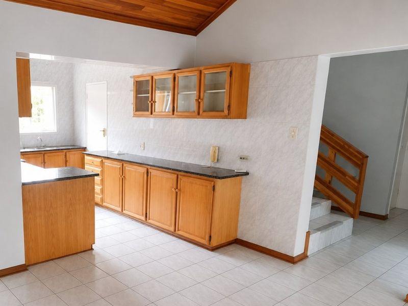 Spacious kitchen featuring wooden cabinetry, granite countertops, tiled flooring, and a vaulted timber ceiling, with an adjacent staircase leading to the upper level.
