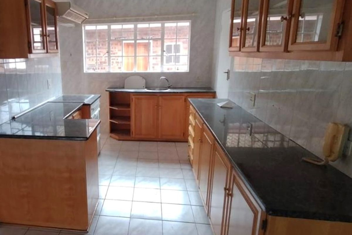A functional kitchen featuring wooden cabinetry, granite countertops, tiled flooring, and a stainless steel sink, offering a clean and practical workspace.