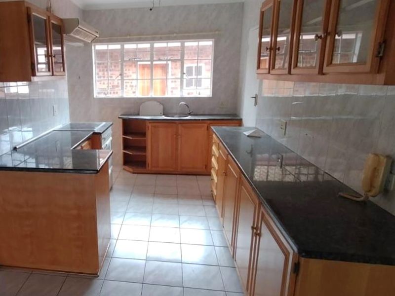 A functional kitchen featuring wooden cabinetry, granite countertops, tiled flooring, and a stainless steel sink, offering a clean and practical workspace.