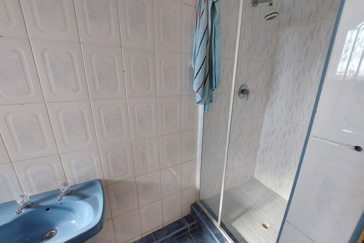 A functional bathroom featuring a shower enclosure with glass door, tiled walls, and a blue pedestal basin.
