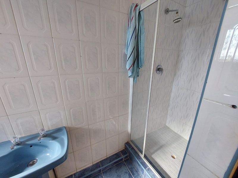 A functional bathroom featuring a shower enclosure with glass door, tiled walls, and a blue pedestal basin.
