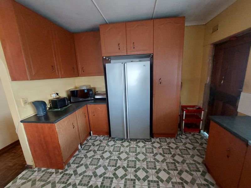 A dated kitchen featuring wood-look laminate cabinetry, dark countertops, and patterned floor tiles, requiring cosmetic updates to modernize the space.