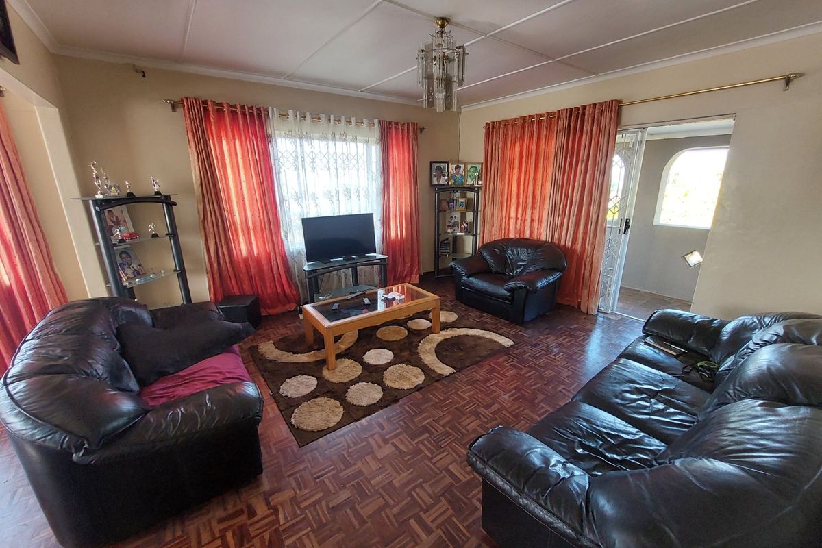 A spacious living room featuring classic parquet flooring, a central chandelier, and large windows with access to an adjacent patio area.