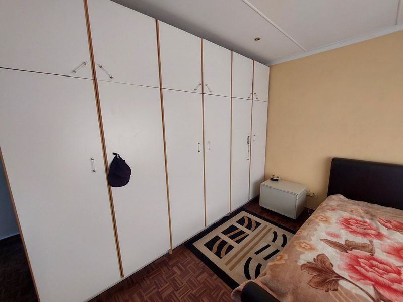 A bedroom featuring extensive built-in white cupboards and classic parquet flooring, offering ample storage space.