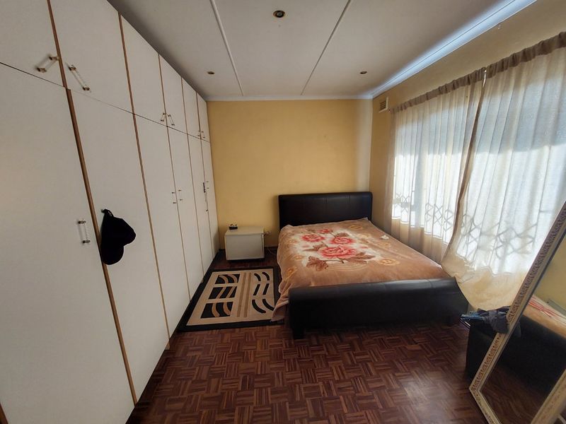 A bedroom featuring parquet flooring, built-in cupboards, and recessed ceiling lighting, offering a functional space with potential for modern updates.