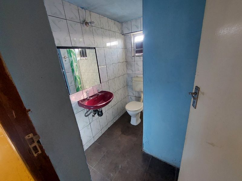 A compact bathroom featuring a wall-mounted basin, toilet, and tiled finishes, presenting an opportunity for modernization and cosmetic updates.