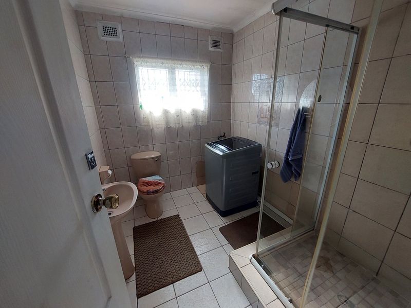 A functional bathroom featuring a pedestal basin, toilet, and a glass-enclosed shower with full-height wall tiling and security bars on the window.