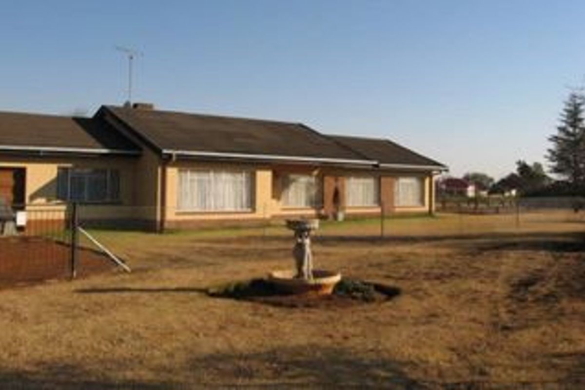 A view of the rear exterior of the residential property, featuring a brick facade, tiled roof, and a central garden fountain on a large lawn.