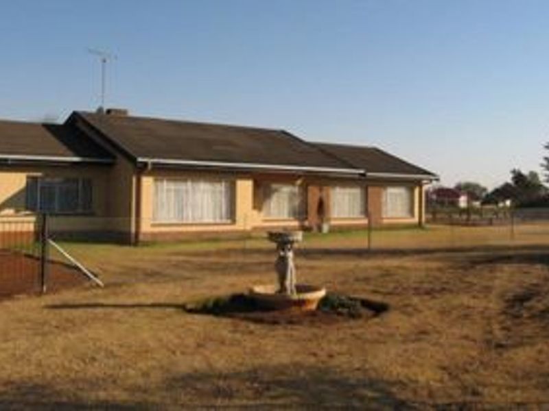 A view of the rear exterior of the residential property, featuring a brick facade, tiled roof, and a central garden fountain on a large lawn.