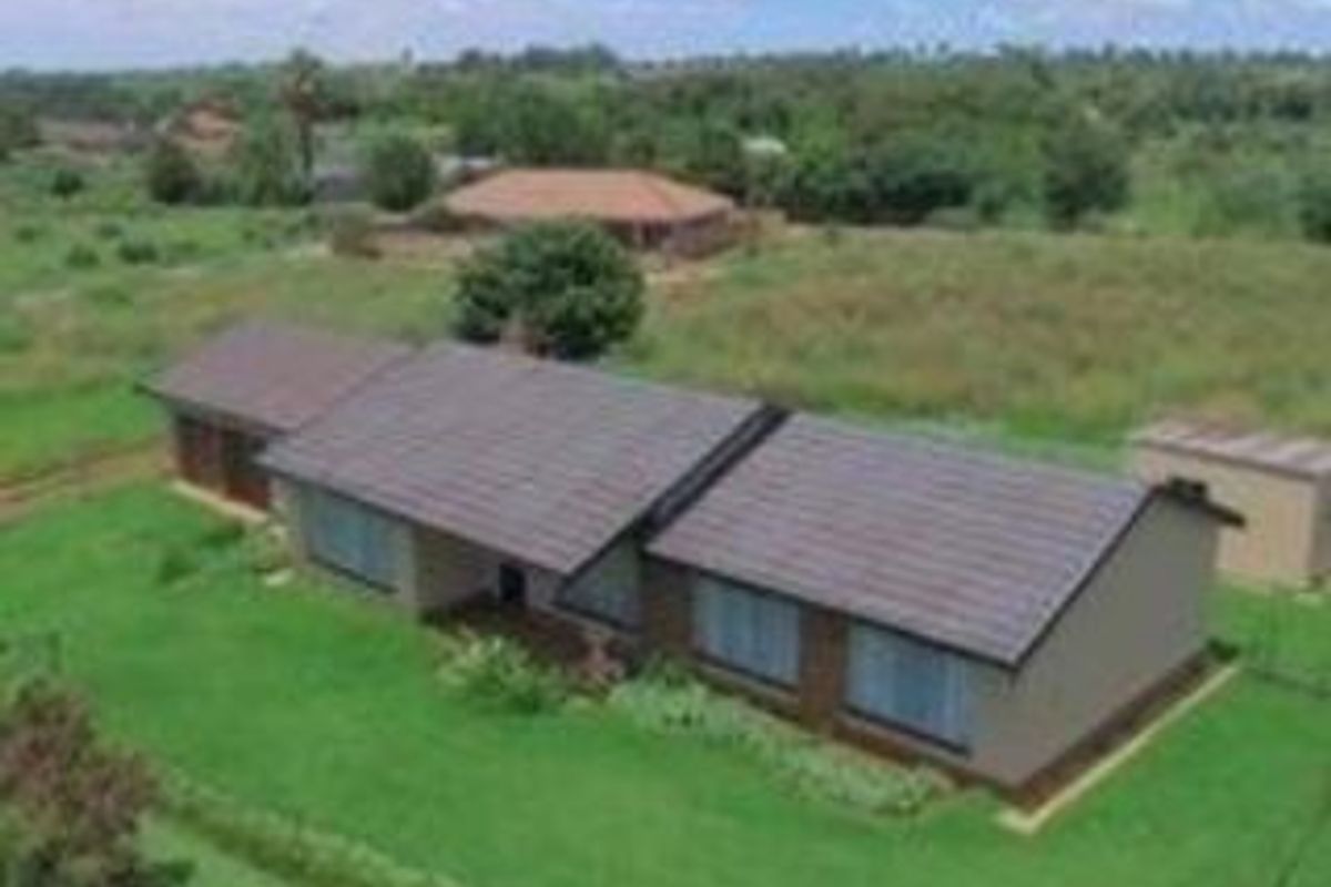 Aerial view of a residential property featuring a tiled roof home set on a large, grassy plot of land.