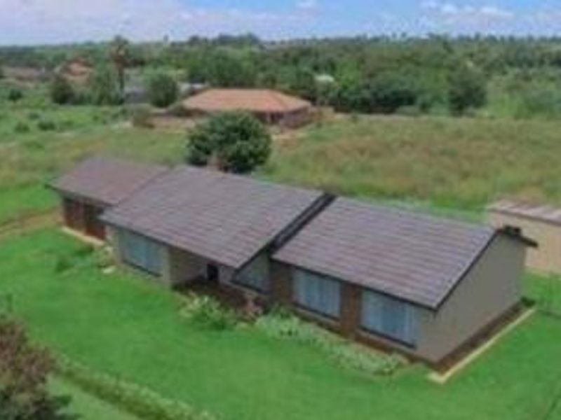 Aerial view of a residential property featuring a tiled roof home set on a large, grassy plot of land.