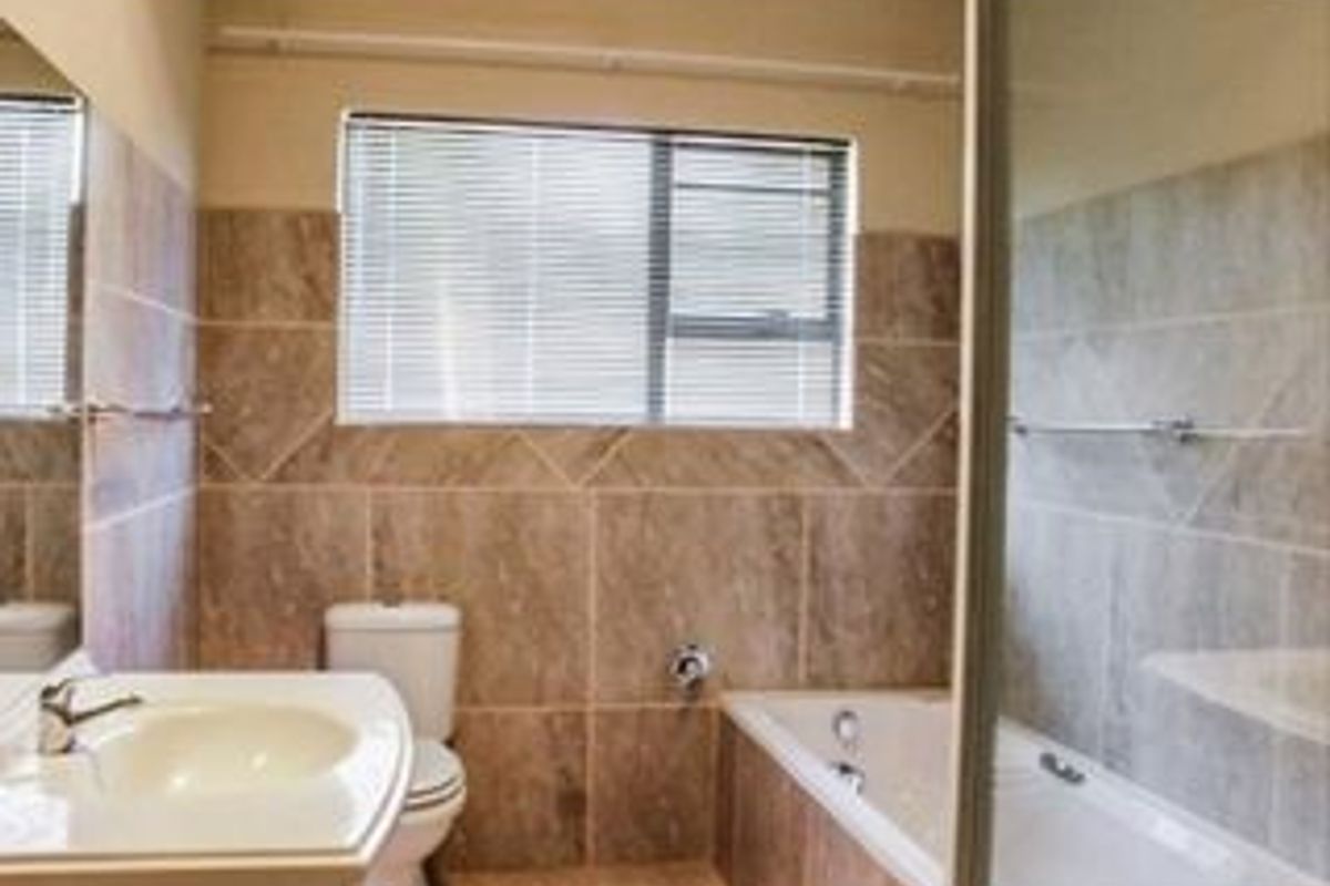 A functional bathroom featuring a vanity basin, toilet, and a combined bathtub and shower area with neutral wall tiling.