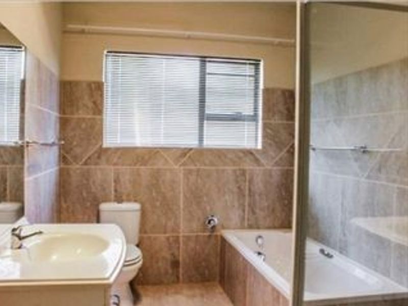 A functional bathroom featuring a vanity basin, toilet, and a combined bathtub and shower area with neutral wall tiling.