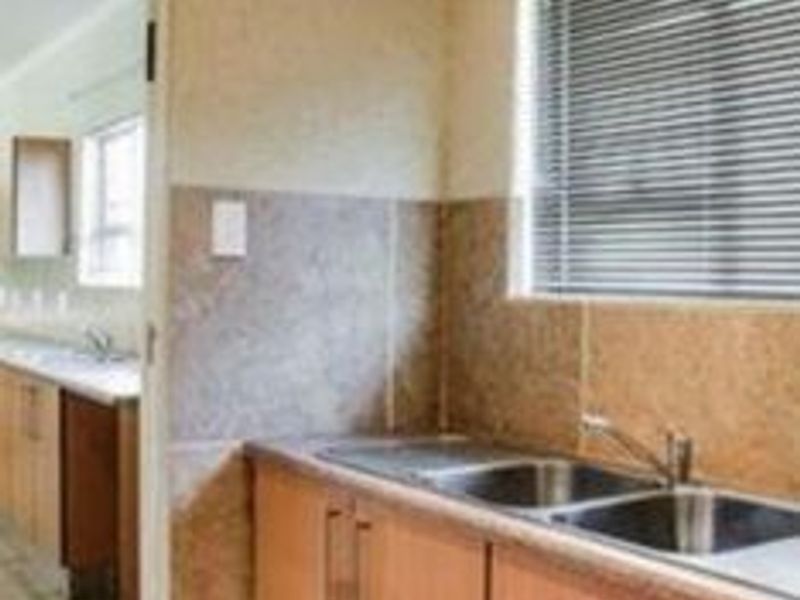A functional scullery area featuring laminate cabinetry, a double bowl stainless steel sink with mixer tap, and tiled splashbacks.